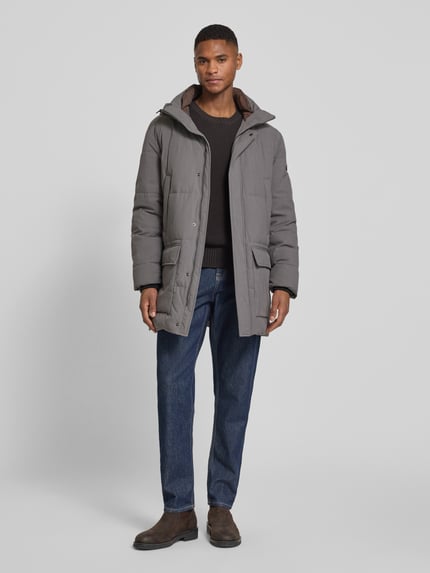 Männermodel trägt Parka mit Kapuze von bugatti in Grau, Regular Fit, verdeckter Reißverschluss, Eingriff- und Pattentaschen. Ganzkörperansicht von vorne.