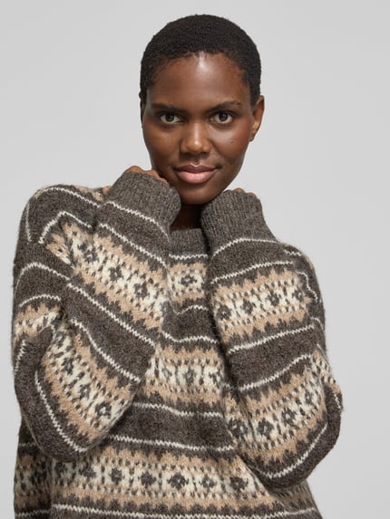 Frauenmodel trägt Pullover mit überschnittenen Schultern Modell 'VMISOLA' von VERO MODA in mehrfarbiger Strickoptik mit Jacquard, geometrischem Allover-Muster, gerippten Abschlüssen und Rundhalsausschnitt, Nahaufnahme Oberkörper.