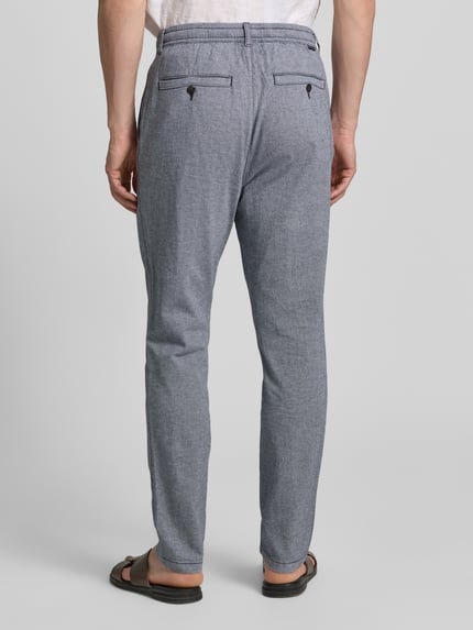 Mężczyznamodel nosi Regular Fit Chino aus Baumwoll-Mix od Tom Tailor, melanż, bawełniany mix, pasujące prosto, z szlufkami, kieszeniami z tyłu i po bokach, z guzikiem i ukrytym zamkiem, widoczny label patch, widok całej sylwetki od tyłu.
