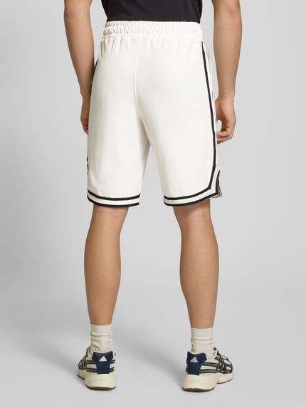 Männermodel trägt Shorts mit Logo-Stitching Modell 'Signar' von Pegador in Weiß mit Kontraststreifen, Reine Baumwolle, Gerader-Schnitt, Ganzkörperansicht Rückansicht.