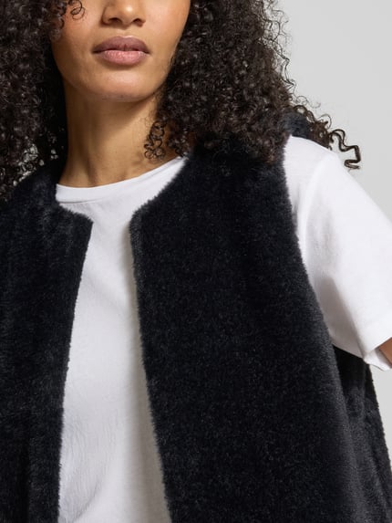 Frauenmodel trägt Regular Fit Weste in Kunstfell-Optik von Tom Tailor, Optik: Unifarben, Hakenverschluss, Label-Stitching-Applikation, Nahaufnahme Oberkörper.