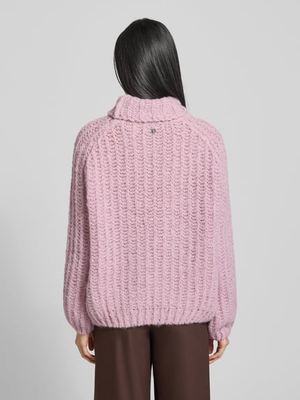Kobieta modelka nosi Strickpullover mit Rollkragen od Smith and Soul, jasnoróżowy, luźny krój, wyraźna faktura prążków, widok całej sylwetki od tyłu. Materiał z domieszką alpaki, długość tyłu 57 cm, długość rękawa 70 cm.