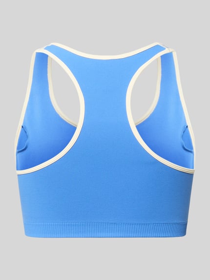 Vrouwenmodel draagt Sport-BH met Logo-Print und Low Support van P.E Nation in blauw met witte accenten, racerback, materiaal-mix met stretch en uitneembare cups, low support, detailopname rugaanzicht.