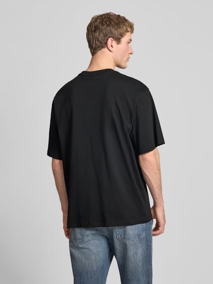 Męski model nosi Oversized T-Shirt mit Logo und Rundhalsausschnitt od The North Face, czarny bawełniany t-shirt, oversize, widok całej sylwetki z tyłu.