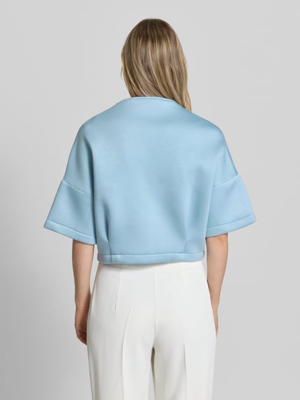Frauenmodel trägt Jacke mit 1/2-Arm und Reißverschlusstaschen von Rinascimento in Hellblau, glatte Textur, gerader Schnitt, Ganzkörperansicht Rückansicht.
