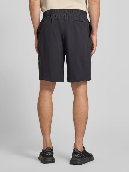 Männermodel trägt Relaxed Fit Cargoshorts mit Label-Schriftzug Modell 'GLOBE CARGO' von BOSS Green in Schwarz, Ganzkörperansicht Rückansicht