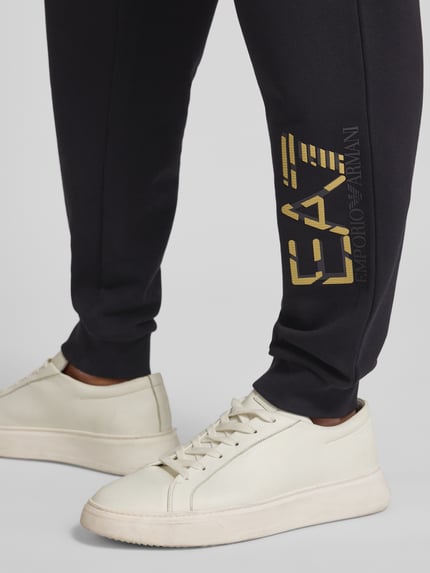 Männermodel trägt Sweatpants mit elastischem Bund und Label-Print von EA7 Emporio Armani, Reine Baumwolle, Regular-Fit, Detailaufnahme Unterschenkel.