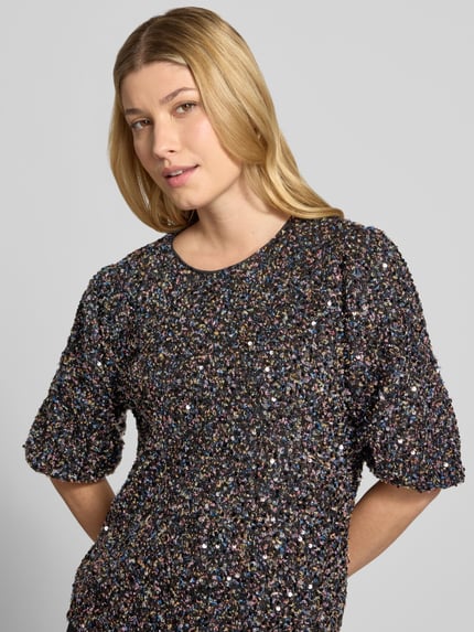 Frauenmodel trägt Kurzarmbluse mit Allover-Pailletten von JAKE*S WOMAN COLLECTION, mehrfarbige Struktur, Rundhals, Nahaufnahme Oberkörper.