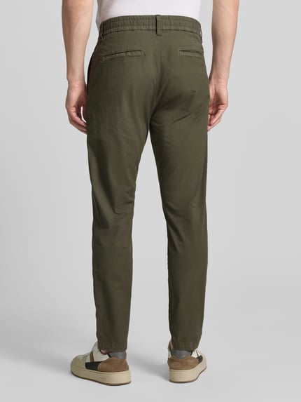 Männermodel trägt Tapered Chino aus Baumwoll-Mix Modell 'CHINO-TAPERED-DS-10' von BOSS Orange in Olivgrün, Baumwollstruktur, Ganzkörperansicht Rückansicht.