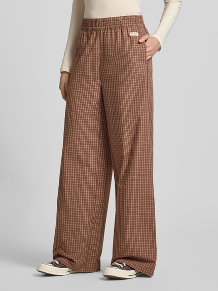 Frauenmodel trägt Wide Leg Hose mit Label-Patch Model 'Hazel' von OH APRIL aus bawełna, spodnie z szerokimi nogawkami, elastyczny pas, szerokość w rozmiarze S: 42 cm, długość wewnętrzna nogawki w rozmiarze S: 79 cm, brązowa krata, tekstura gładka, całkowity widok z przodu