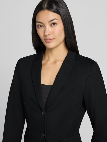 Frauenmodel trägt Slim Fit Blazer aus Viskose-Elasthan-Mix von Marc Cain mit Reverskragen, 2-Knopfverschluss, Pattentaschen, Nahaufnahme Oberkörper, Rückenlänge bei Größe 36: 56 cm, Brustweite: 23 cm, Ärmellänge: 63 cm.