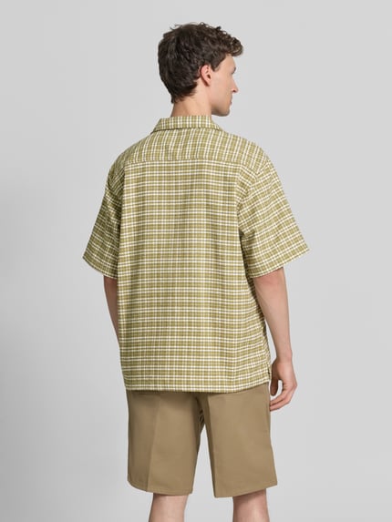 Männermodel trägt Regular Fit Freizeithemd aus reiner Baumwolle von Carhartt Work In Progress mit Strukturmuster, kariert, Halbarm, Ganzkörperansicht Rückansicht. Rückenlänge bei Größe M: 74 cm, Schulterbreite bei Größe M: 49 cm, Ärmellänge bei Größe M: 29 cm, durchgehende Knopfleiste, Brand-Stitching.