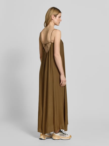 Frauenmodel trägt Maxikleid mit Spaghettiträgern und Karree-Ausschnitt von Style Icon Collection in Braun, lockerem Schnitt, Rückseite mit Schlüsselloch-Ausschnitt und Bindung, fließende Textur, Ganzkörperansicht Rückansicht. Kontext: Damen Maxikleid, Brustweite bei Größe 36: 27 cm.