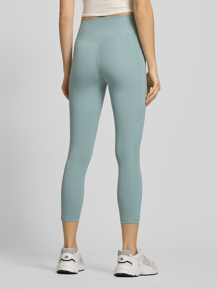 Frauenmodel trägt Leggings mit Logo und elastischem Bund von adidas Sportswear in Hellblau, figurbetont, elastischer Bund, Ganzkörperansicht Rückansicht.