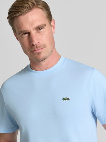 Männermodel trägt Regular Fit T-Shirt aus reiner Baumwolle von Lacoste in Hellblau, glatte Textur, Herren T-Shirt, Nahaufnahme Oberkörper.
