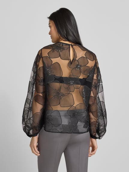 Frauenmodel trägt Bluse in transparenter Optik mit Rundhalsausschnitt von Luisa Cerano im Allover-Look, Regular-Fit, Rückenlänge 61 cm, Ärmellänge 58 cm, schwarze Blüten, lockere Textur, Ganzkörperansicht Rückansicht.