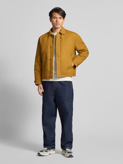 Männermodel trägt Jacke mit Label-Stitching und Eingrifftaschen von BLKVIS in Senfgelb, reine Baumwolle, Regular Fit, Ganzkörperansicht von vorne.