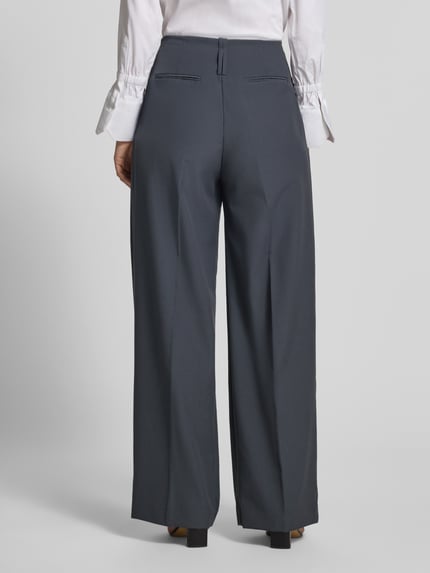 Frauenmodel trägt Wide Fit Hose mit Viskose-Anteil Modell 'Dario' von MANGO in Dunkelgrau mit Bundfalten, Ganzkörperansicht Rückansicht.