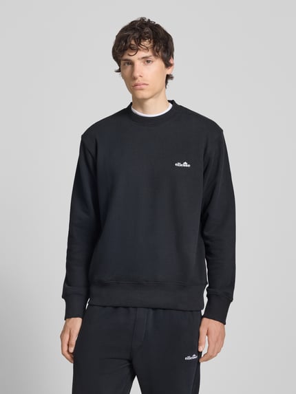 Männermodel trägt Sweatshirt mit Rundhalsausschnitt und Label-Stitching von Ellesse, schwarze Farbe, Regular Fit, Baumwoll-Mix, Ganzkörperansicht von vorne