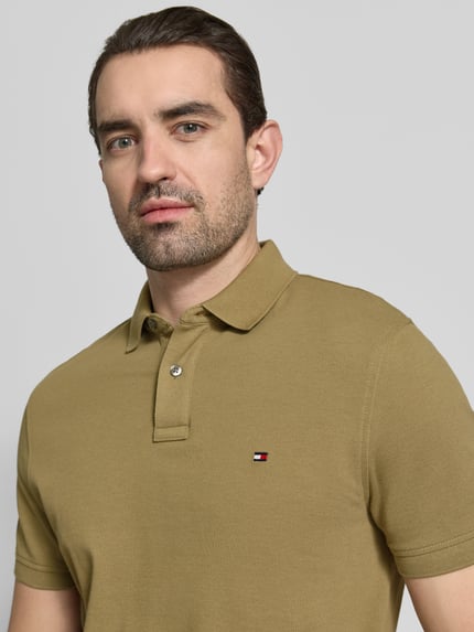 Męski model nosi Regular Fit Poloshirt aus Baumwoll-Mix od Tommy Hilfiger, efekt: jednolity kolor, wyhaftowane logo, kołnierzyk polo, zapięcie na 2 guziki, krótki rękaw, wykończenie: z rozcięciem, wykończenie materiału: pika, mieszanka bawełny, nahaufnahme górnej części ciała.