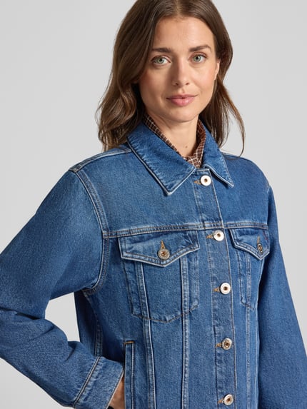 Frauenmodel trägt Jeansjacke mit Brusttaschen Modell 'Saima' von MOS MOSH aus reiner Baumwolle in Blau, strukturierte Oberfläche, Nahaufnahme Oberkörper.