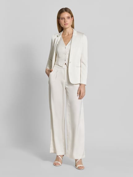 Modelka nosi Weste aus Satin mit V-Ausschnitt von Jake*s Cocktail, satyna, krój slim fit, dekolt w serek, listwa guzikowa, kieszenie z wypustkami, długość tyłu w rozmiarze 36: 40 cm, jasny kolor, gładka faktura, Ganzkörperansicht von vorne.