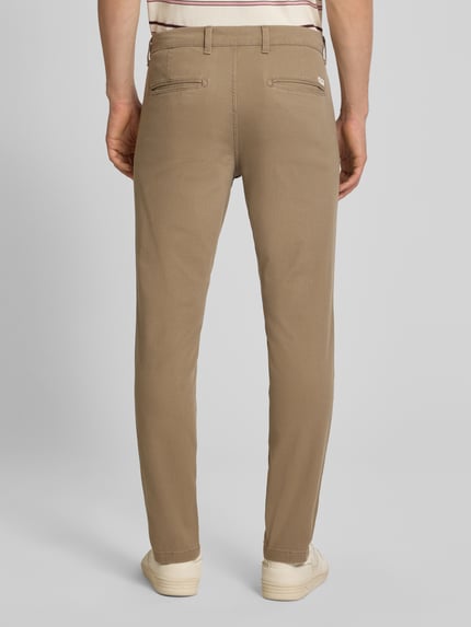 Męski model nosi Slim Fit spodnie z kieszeniami z tyłu Model 'MARCO' od Jack & Jones, mieszanka bawełny i elastanu, krój slim fit, Szerokość w rozmiarze 32/32: 43 cm, Długość wewnętrzna nogawki: 77 cm, beżowy kolor, tekstura gładka, widok całej sylwetki z tyłu.