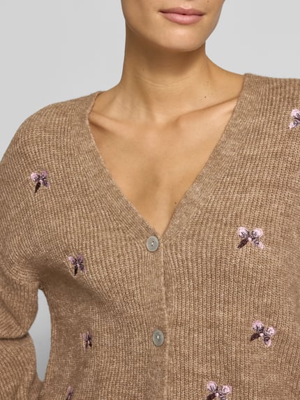 Frauenmodel trägt Relaxed Fit Strickjacke aus elastischem Woll-Mix Modell 'FLEUR' von YAS, braune Farbe, florale Stickerei, Nahaufnahme Oberkörper.