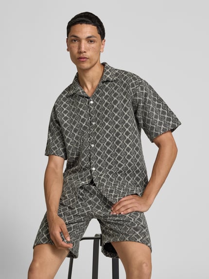 Männermodel trägt Boxy Fit Freizeithemd im Allover-Look Modell 'ZANDER' von Redefined Rebel, Reine Baumwolle, Reverskragen, Ganzkörperansicht von vorne. Rückenlänge bei Größe M: 65 cm, Schulterbreite bei Größe M: 51 cm, Ärmellänge bei Größe M: 25 cm.