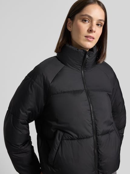 Frauenmodel trägt schwarze Pufferjacke mit Stehkragen Modell 'VMBRENDA' von VERO MODA, Steppstruktur, elastische Abschlüsse, Nahaufnahme Oberkörper.