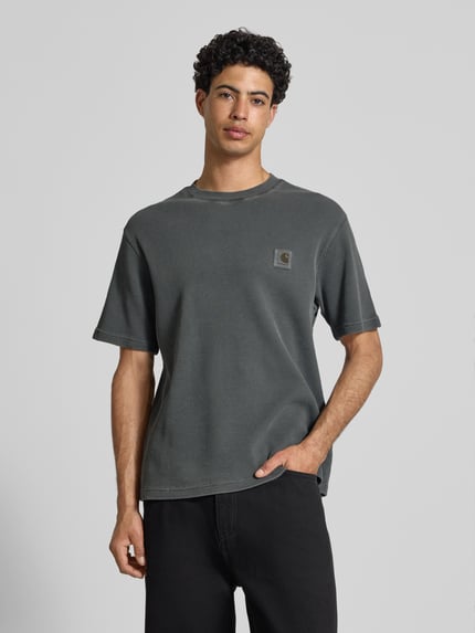 Mannelijk model draagt T-shirt met structuurpatroon model 'Nelson' van Carhartt Work In Progress, zuiver katoen, relaxed fit, labeldetail, ronde hals, ruglengte maat M 70 cm, donkergrijs met fijne textuur, relaxed silhouet, voorkant bovenlichaam close-up.