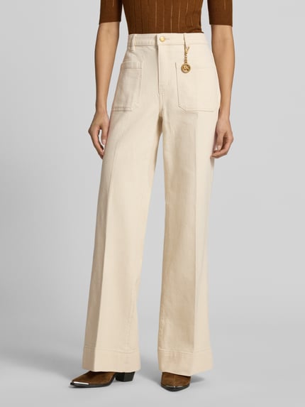 Frauenmodel trägt High Rise Bootcut Fit Stoffhose aus Baumwoll-Mix von MICHAEL Michael Kors in Beige mit aufgesetzten Eingrifftaschen, Label-Anhänger in metallic, weit geschnittenes Bein, Struktur fein, Nahaufnahme Oberkörper.