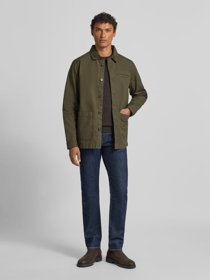 Męski model nosi Regular Fit Hemdjacke aus reiner Baumwolle von Barbour, efekt: jednolity kolor, krój regular fit, wykładany kołnierz z obszyciem ze sztruksu, listwa guzikowa, wyhaftowane logo, długi rękaw z mankietem, wpuszczane kieszenie, materiał: czysta bawełna, kolor oliwkowy, całopostaciowy widok z przodu.