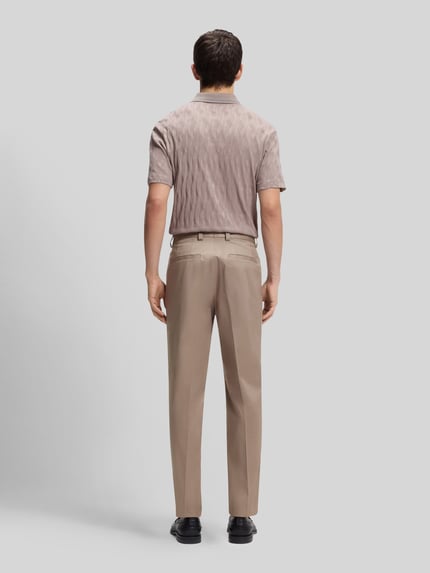 Männermodel trägt Slim Fit Bundfaltenhose aus Baumwoll-Mix Modell 'GENRICH' von HUGO, efekt: jednolity kolor, krój slim fit, aplikacja z marką, zakładki w pasie, szlufki na pasek, kanty, zapięcie na haftkę i zamek błyskawiczny, wpuszczane kieszenie, kieszenie z tyłu z guzikiem, mieszanka bawełny, Ganzkörperansicht Rückansicht.