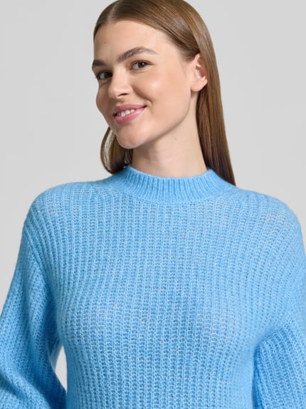 Frauenmodel trägt Pullover mit Ballonärmeln Modell 'Siforo' von HUGO in hellblauer Strickoptik, Strukturmuster, Rundhals, Nahaufnahme Oberkörper.
