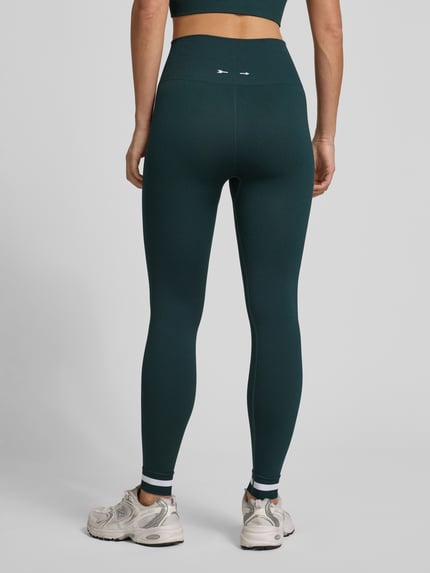 Modelka kobieca nosi Regular Fit Leggins mit breitem Bund von The Upside, zielony kolor, elastyczny materiał, szeroki pas, widok całej sylwetki z tyłu.