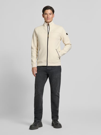 Männermodel trägt Sweatjacke mit Label-Patches und Stehkragen von PME Legend, cremefarben, Reißverschluss, seitliche Taschen, Ganzkörperansicht von vorne. Baumwoll-Mix mit Stretch-Anteil, Straight Fit, gerippte Abschlüsse, Rückenlänge 73 cm, Ärmellänge 68 cm.