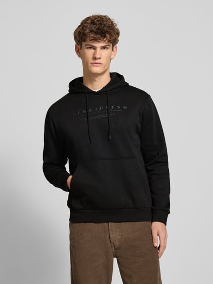 Männermodel trägt Hoodie mit Label-Print von Jack & Jones in Schwarz aus Baumwoll-Mix, Känguru-Tasche, lockerer Schnitt, Nahaufnahme Oberkörper.