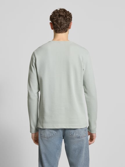 Mężczyzna nosi Regular Fit Langarmshirt aus Baumwoll-Mix Modell 'TEMPESTO' od BOSS Orange w jasnoszarym kolorze, tekstura piqué, gładki wzór, długi rękaw, widoczne label-stitching, widok całej sylwetki z tyłu.