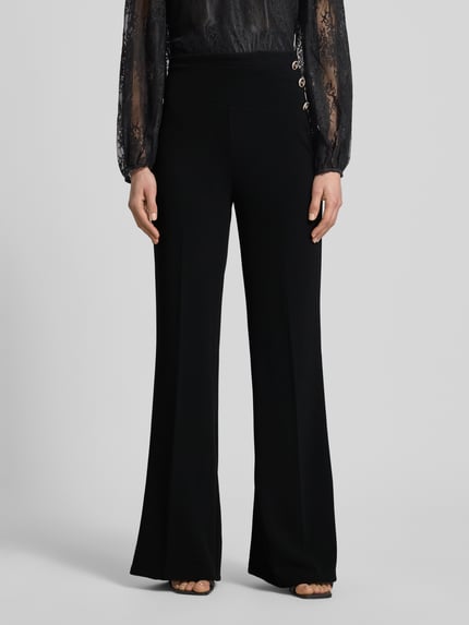 Frauenmodel trägt Flared Cut Hose mit Knöpfen von Rinascimento, schwarz, Material-Mix mit Stretch, Nahaufnahme Oberkörper bis Fuß.