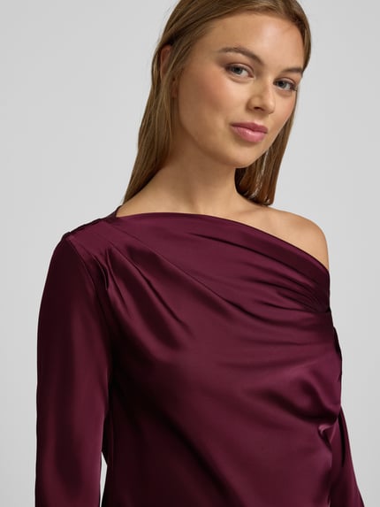 Frauenmodel trägt Regular Fit Bluse im One-Shoulder-Look Modell 'HASBRIN' von Lauren Ralph Lauren aus glänzendem Satin in Dunkellila, Nahaufnahme Oberkörper, Damen Bluse mit Rückenlänge 52 cm und Ärmellänge 63 cm bei Größe S.