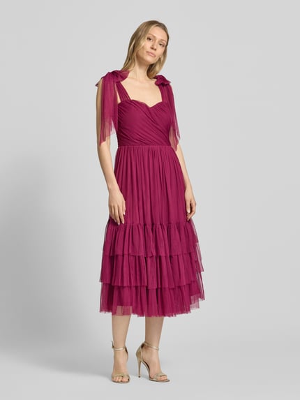 Frauenmodel trägt knielanges Cocktailkleid im Stufen-Look von LACE & BEADS aus Mesh in A-Linie mit Drapierungen, Ganzkörperansicht von vorne. Rückenlänge bei Größe S: 104 cm, Brustweite bei Größe S: 40 cm.