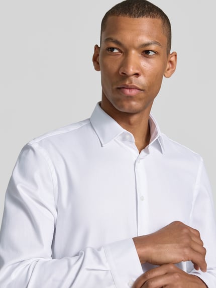 Männermodel trägt Super Slim Fit Business-Hemd mit Kentkragen von Jake*s aus Reine Baumwolle in Weiß, feine Textur, Nahaufnahme Oberkörper. Rückenlänge 79 cm, Schulterbreite 46 cm, Ärmellänge 66 cm, Knopfleiste, Sportmanschetten, abgerundeter Saum, Größe 39/40.