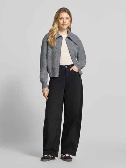 Modelka kobieca ma na sobie Regular Fit Strickjacke mit Zweiwege-Reißverschluss Modell 'Teski' od someday., szary melanż, prążkowana faktura, długi rękaw, stójka, z przodu zamek błyskawiczny, krój regular fit, Szerokość w rozmiarze 36: 45 cm, Długość z tyłu w rozmiarze 36: 52 cm, Szerokość klatki piersiowej w rozmiarze 36: 57 cm, Długość rękawa w rozmiarze 36: 70 cm, pełen widok z przodu.
