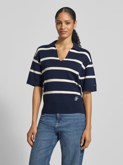 Frauenmodel trägt Regular Fit Pullover aus reiner Baumwolle von Tommy Hilfiger, dunkelblau mit weißen Streifen, feiner Strick, Logo-Stitching, Polokragen und V-Ausschnitt, kurzarm, gerippte Abschlüsse, Ganzkörperansicht von vorne.