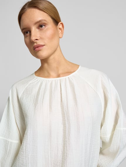 Frauenmodel trägt Blusenshirt mit Raglanärmeln Modell 'Fibiza' von OPUS, weiß, Lyocell-Mix, lockerer Schnitt, Nahaufnahme Oberkörper.