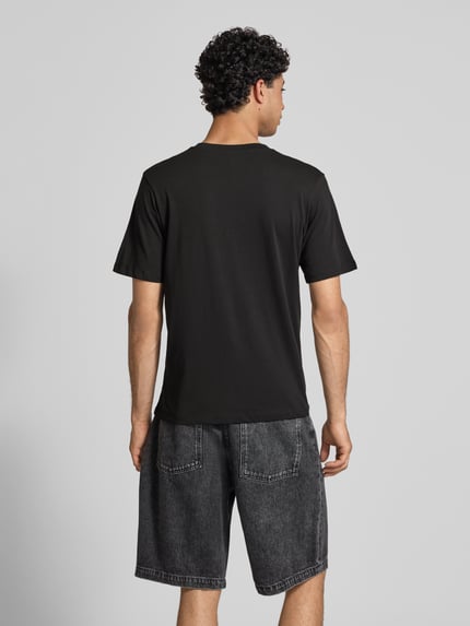 Męski model nosi t-shirt z nadrukiem z napisem model 'RHYERES' od Jack & Jones z woskowanej bawełny, krój regular fit, okrągły dekolt, długość tyłu w rozmiarze m: 67 cm, widok całej sylwetki od tyłu.