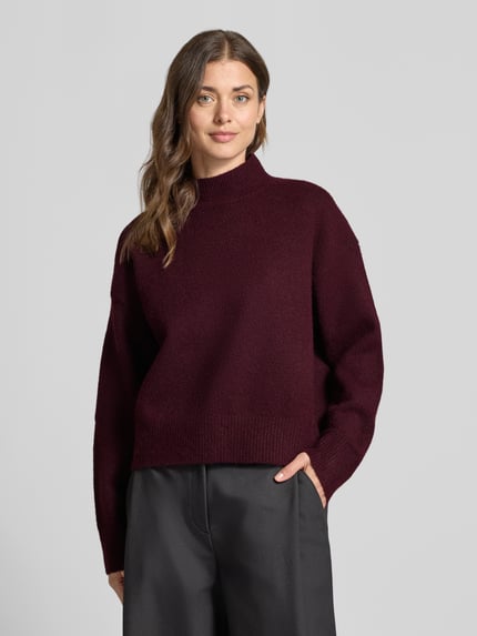 Frauenmodel trägt Turtleneck-Pullover mit Woll-Anteil und Rundhalsausschnitt von Neo Noir, weinrote Farbe, gerader Schnitt, Nahaufnahme Oberkörper.
