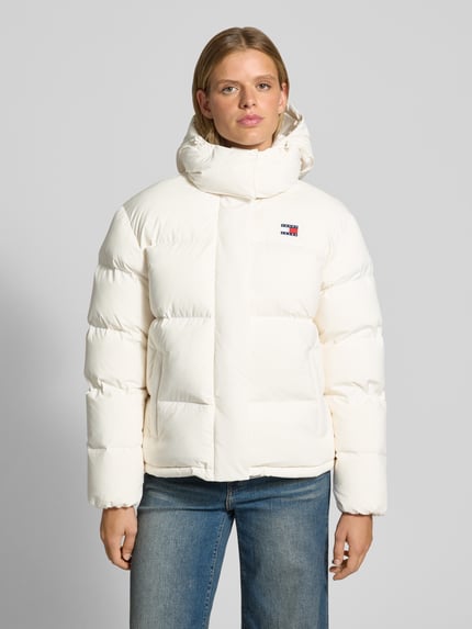 Frauenmodel trägt Regular Fit Steppjacke mit abnehmbarer Kapuze von Tommy Jeans, cremeweiß, klare Steppung, Jeans, Ganzkörperansicht von vorne, Damen Steppjacke von Tommy Jeans.