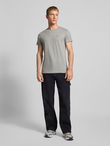 Männermodel trägt T-Shirt in Melange-Optik von Tommy Jeans aus reiner Baumwolle, gerader Schnitt, Logo-Stitching, Ganzkörperansicht von vorne.